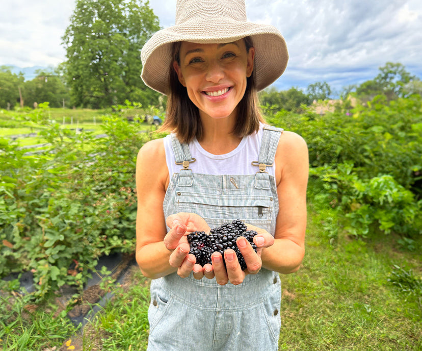 Jennifer Garner holding blackberries in an outdoor setting with greenery